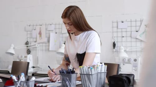 Young Beautiful Woman Drawing Sketch of Female Dress in Sewing Studio