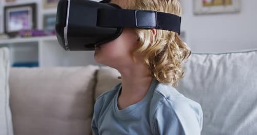 Caucasian boy gesturing while using vr headset sitting on the couch at home