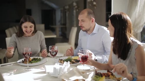 Male in the Company of Two Charming Ladies at the Restaurant Offers to Raise a Glass with Red Wine