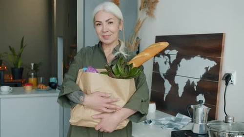 Mature Woman Holds Groceries in Modern Kitchen