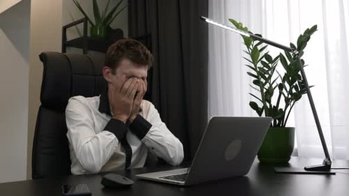 Tired overworked man is rubbing eyes in business office.