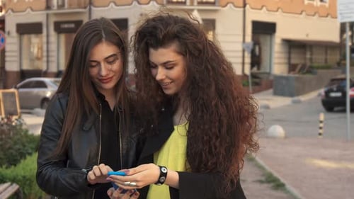 Two Women Looking at a Phone in the City