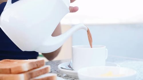 Woman is Pouring a Coffee with Milk From Teapot to White Cup Closeup