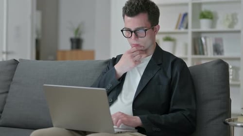 Nachdenklicher junger männlicher Designer denkt und arbeitet zu Hause am Laptop