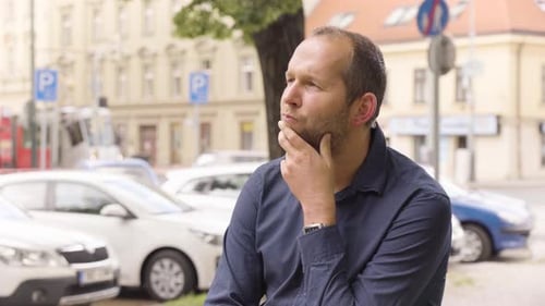 A Caucasian Man Thinks About Something in an Urban Area a Colorful Street in the Blurry Background
