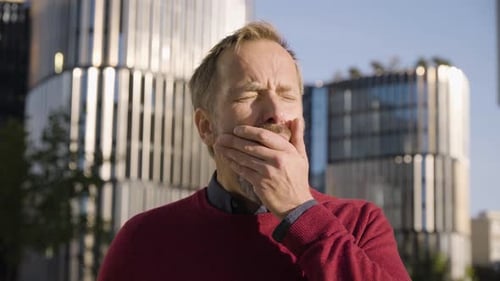 A Middleaged Handsome Caucasian Man Yawns and Looks at the Camera in an Urban Area