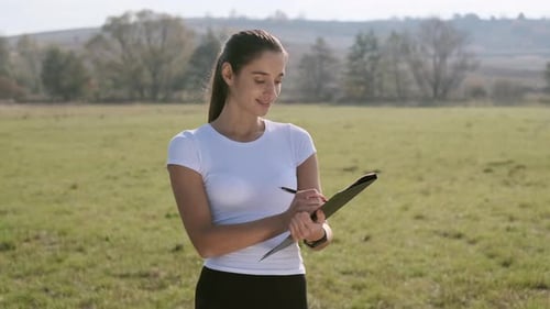 Woman Writing on Clipboard in Rural Grassy Field
