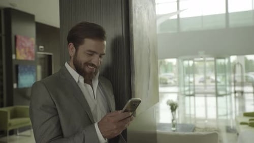 Bearded Man Smiling Using Phone in Lobby