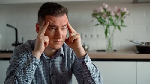 Stressed Man Massaging Temples in Kitchen