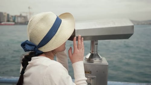 Woman Looks Through Binoculars Exploring Coast on Embankment