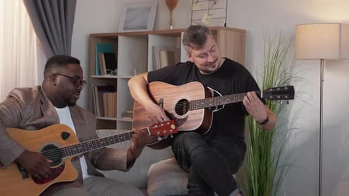 Two Friends Play Acoustic Guitars on Sofa