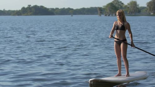 A young woman sup stand-up paddleboarding on a lake.