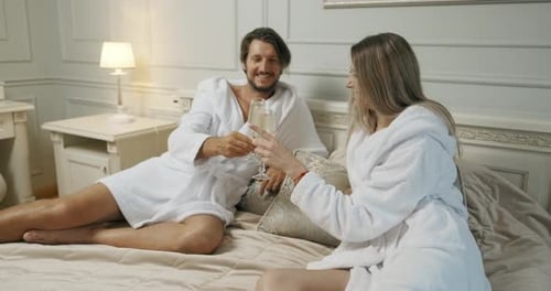 Affectionate Couple Toasting with Champagne Lying on Their Bed. Hotel, Travel, Relationships and