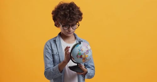 Clever Schoolboy in Glasses Exploring Earth Globe, Orange Studio Background