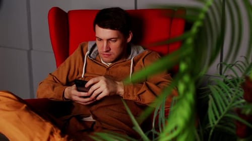 Mann sitzt im Sessel mit Smartphone