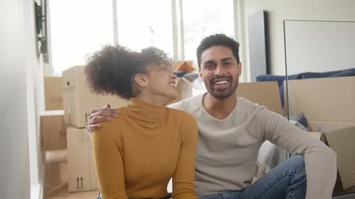 Portrait Of Happy Couple In Lounge Of New Home With Keys On Moving Day Surrounded By Removal Boxes