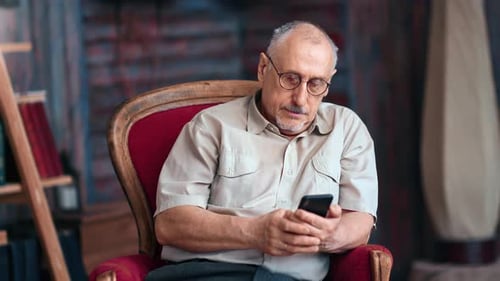 Senior Man Looking at Mobile Phone Sitting in Chair