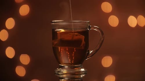 Schwarzer Teerücken, der in einen dampfenden Glasbecher vor einer wunderschönen Bokeh-Kulisse getaucht wird.