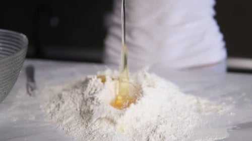 Closeup View of Female Hands Breaking the Second Egg Into Flour on the Kitchen Table