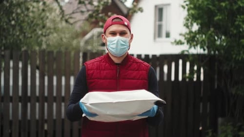 Delivery Concept Portrait of Happy Spanish Delivery Man with Face Mask in Red Cloth Holding a Box