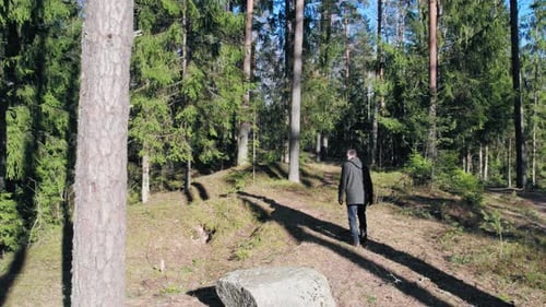 Ein junger Mann in dunklen Kleidern mit kurzen Haaren geht durch den Wald