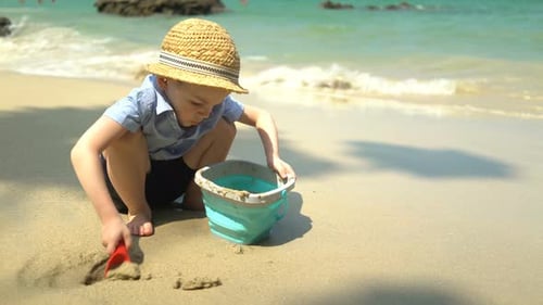Boy Playing on the Beach By the Sea. He Digs Sand and Throws It in the Bucket