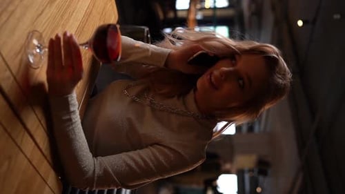 Vertical Portrait of Beautiful Blonde Young Woman Sitting in Restaurant Alone Talking on Mobile