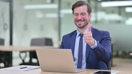 Man Gives Thumbs Up at Office Desk with Laptop