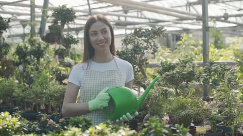 Woman Smiling with Watering Can in Greenhouse