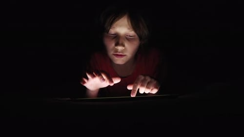 Enfant jouant à un jeu sur tablette la nuit