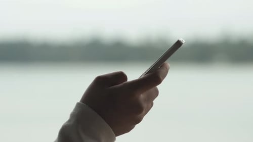 Hand Holding Cell Phone by Water