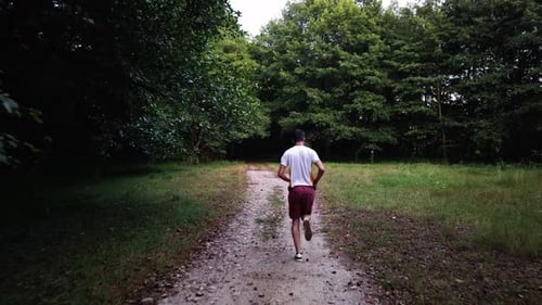 Young Caucasian male running in forest on a trail in summer. Man jogging cross country running on tr