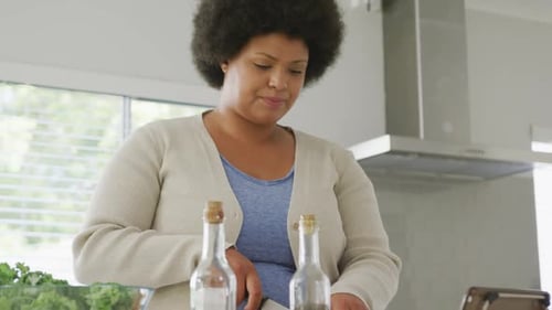 Video of plus size african american woman using tablet, preparing meal