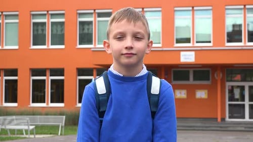 A Young Boy Looks Seriously at the Camera - an Elementary School in the Background