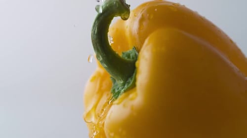 Water drops on rotating yellow pepper. Slow Motion.