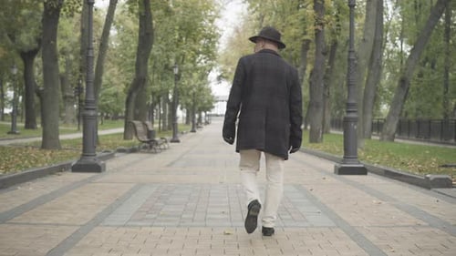 Wide Shot of Confident Caucasian Adult Man Strolling Along Park Alley on Cloudy Autumn or Spring Day