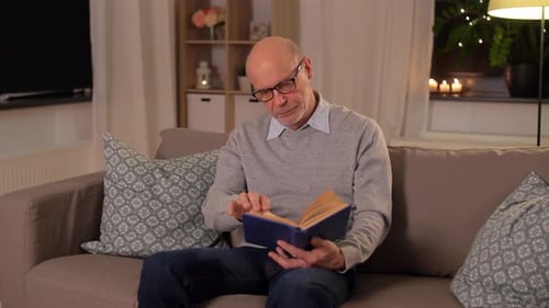 Bald Senior Man on Sofa Reading Book at Home