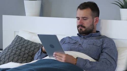 Man Resting in Bed Using Tablet Device