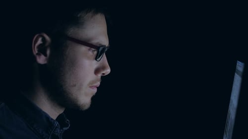 Mann mit Brille arbeitet nachts am Laptop