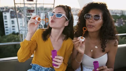 Young Women Blowing Bubbles on Amusement Park Ride