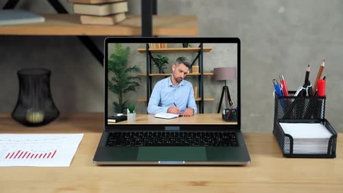 Laptop Standing on Table Display with Businessman in Office Writes in Notebook