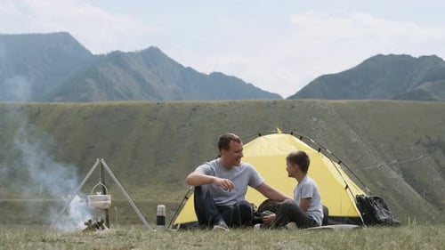 Father and Son Are Sitting Near the Tent and Bonfire and Laughing