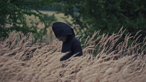 Dark ghost in black cloak with hood among nature.
