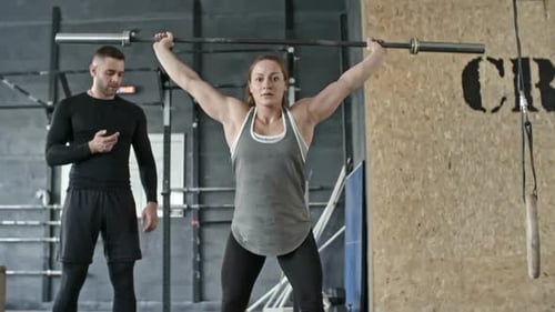 Woman lifting barbell with coach in gym