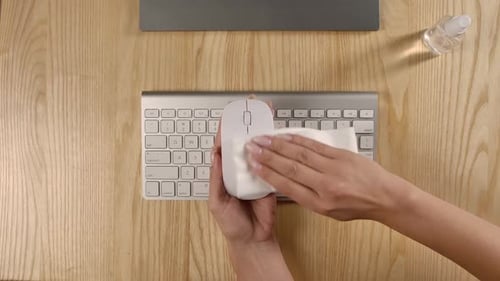 An Overhead View of Female Hands Cleaning a Computer Mouse with an Antibacterial Disinfectant Wipe