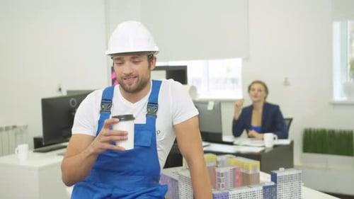 Construction Worker Drinks Coffee Near Building Model