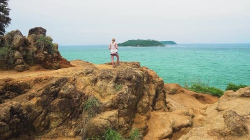 tourist girl is standing on the stone coast of the sea and looking