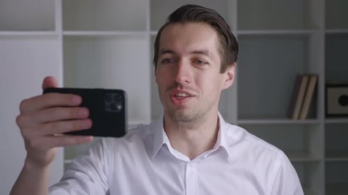 Portrait of Happy Businessman Making Facetime Video Calling with Smartphone at Modern Office Waving