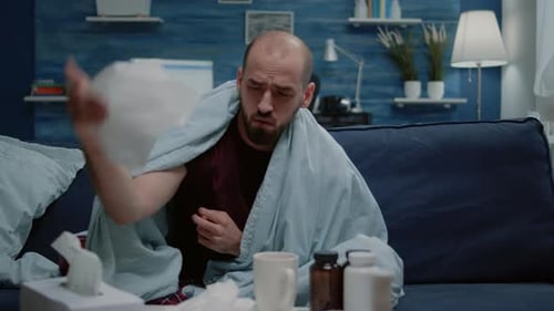 Sick Man Sitting on Couch Blowing Nose