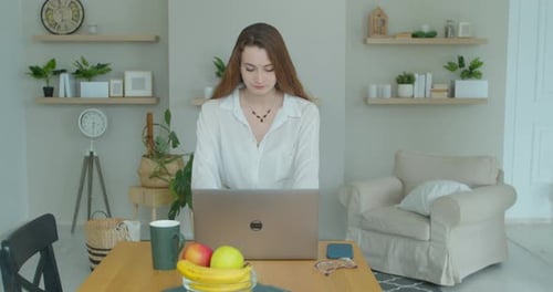 Woman Works at Laptop and Drinks Coffee at Home